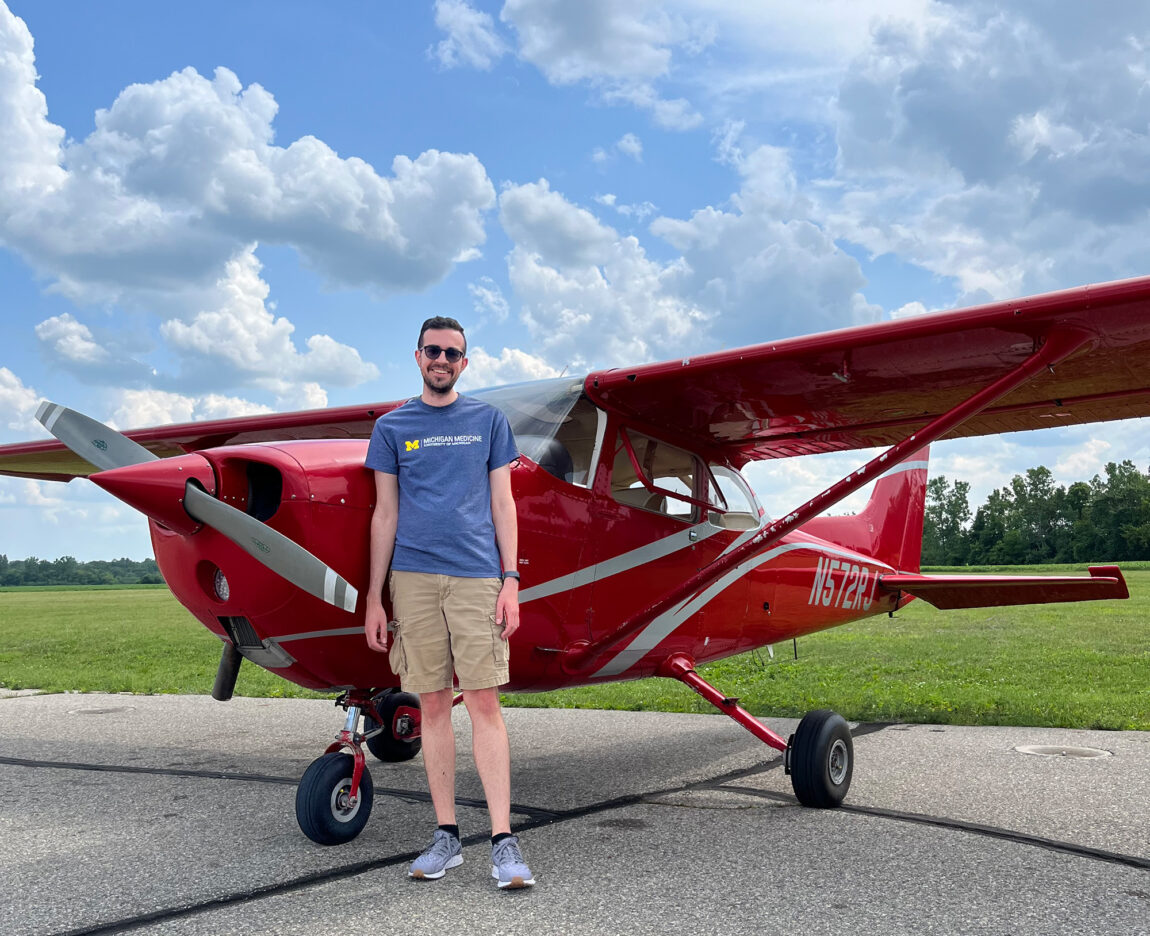 A man stands in front of a small red airplane