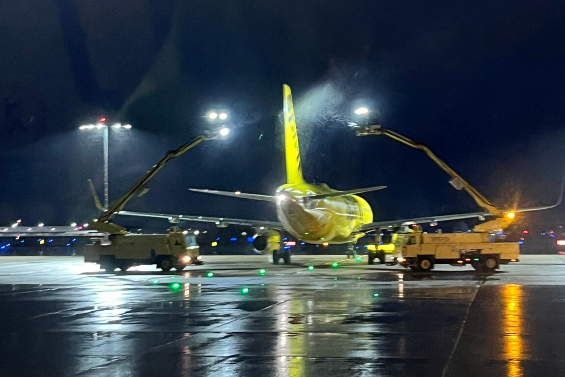 A plane is de-iced by two vehicles on a dark runway