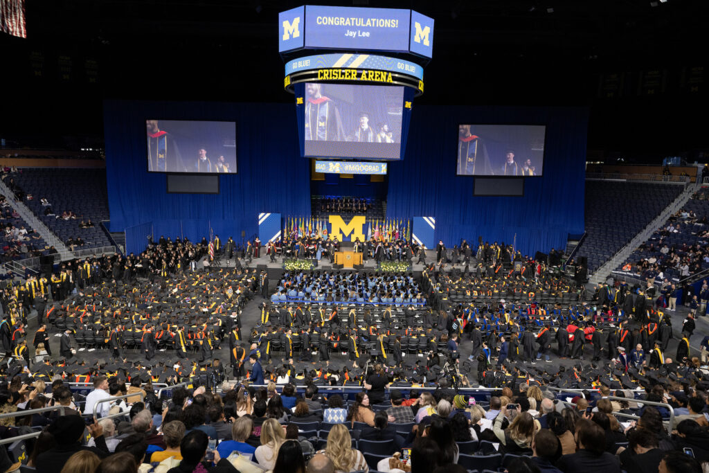 An overview shot of a graduation ceremony in an arena showing people seated facing a stage
