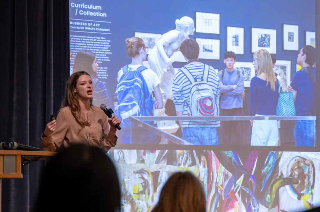 A woman presents in front of a large screen