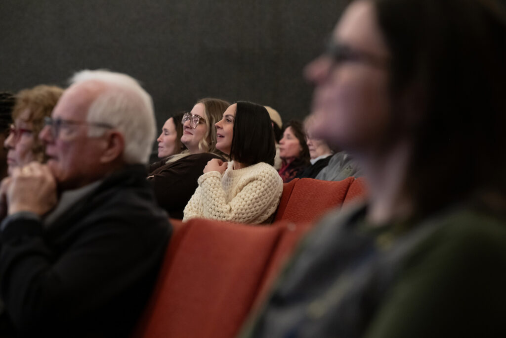 People sitting in an auditorium look toward a stage