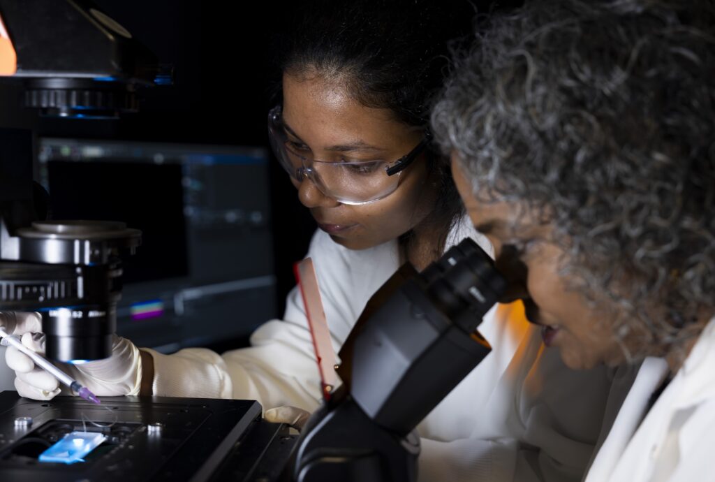 Abha Kumari positions the GlioExoChip chip on the microscope while Sunitha Nagrath looks through the eyepiece. Extracellular vesicles captured from tumor cells could be used to discover whether a brain cancer treatment is working, the U-M/Northwestern study showed. Image credit: Jeremy Little/Michigan Engineering
