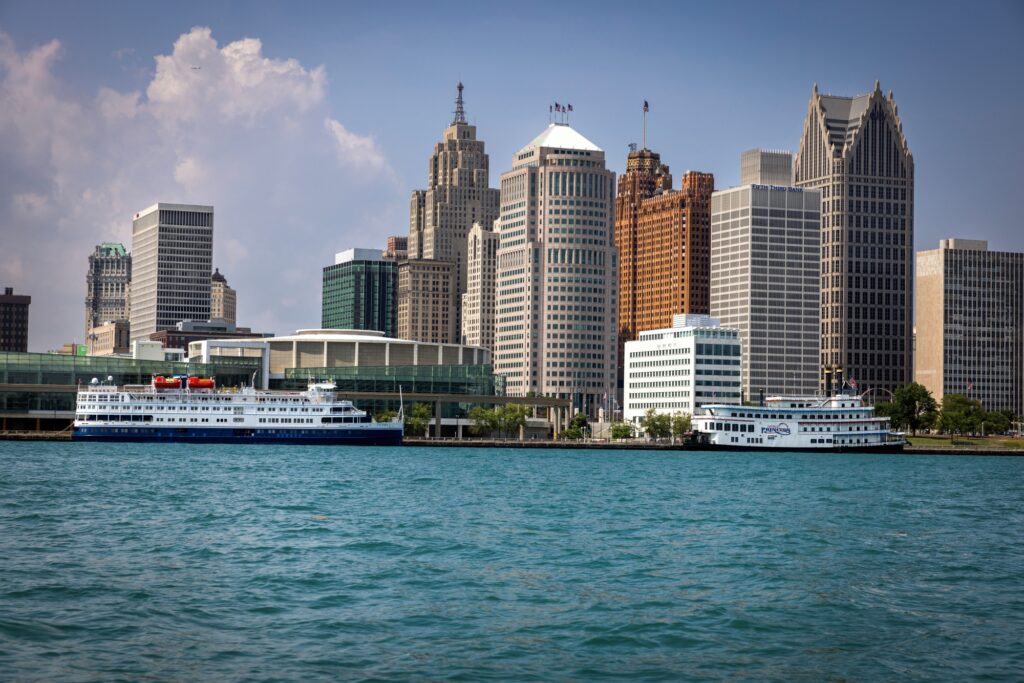 Skyscraper tower over two long, white cruise ships in the light blue river.