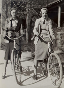 Two young Michigan students, caucasian females, on bicycles on the Ann Arbor campus, circa