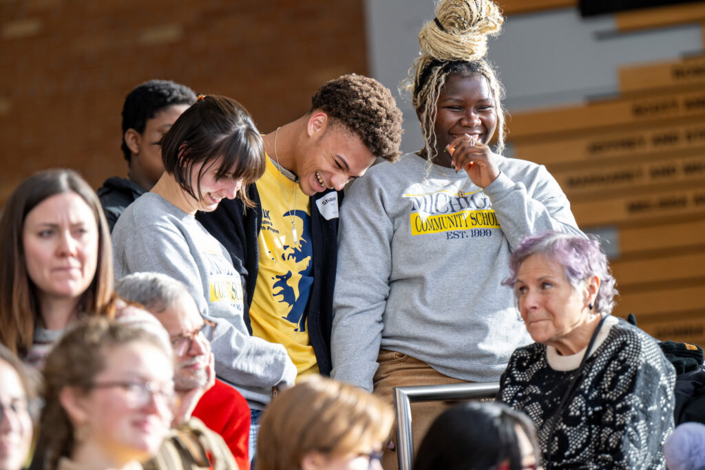People stand next to each other and smile and laugh while attending an event
