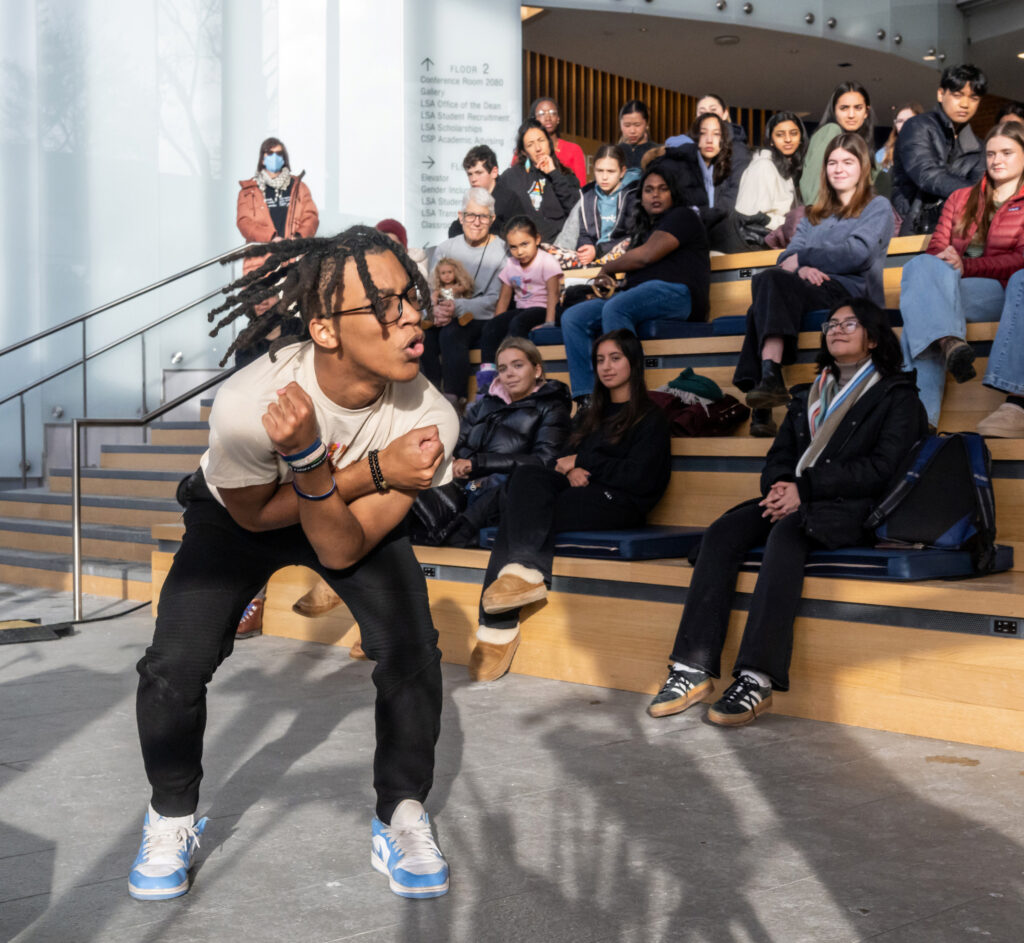 A man performs a dance routine while people seated on risers watch