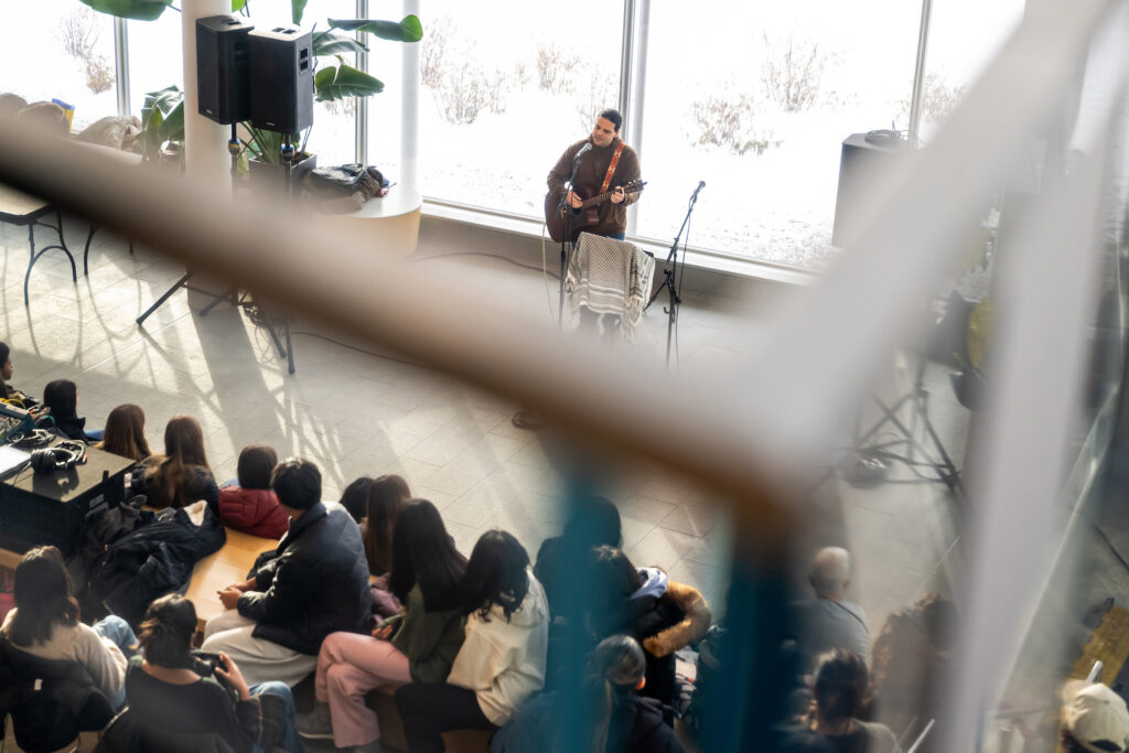 An overhead view of a man playing guitar in front of dozens of people seated nearby