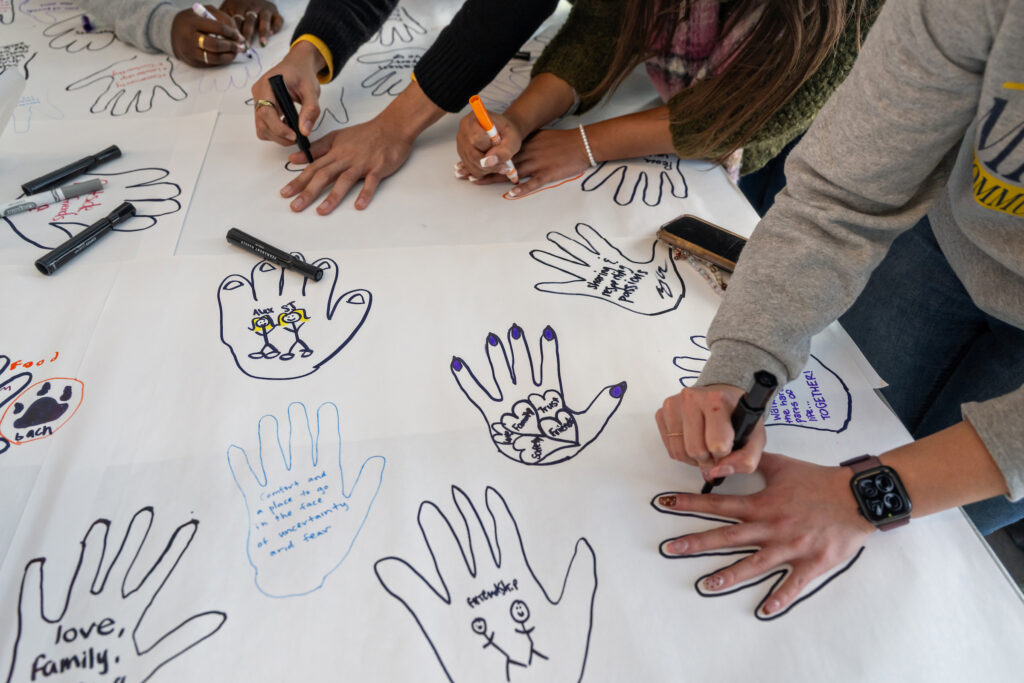 People trace their hands with markers and write messages inside the shape