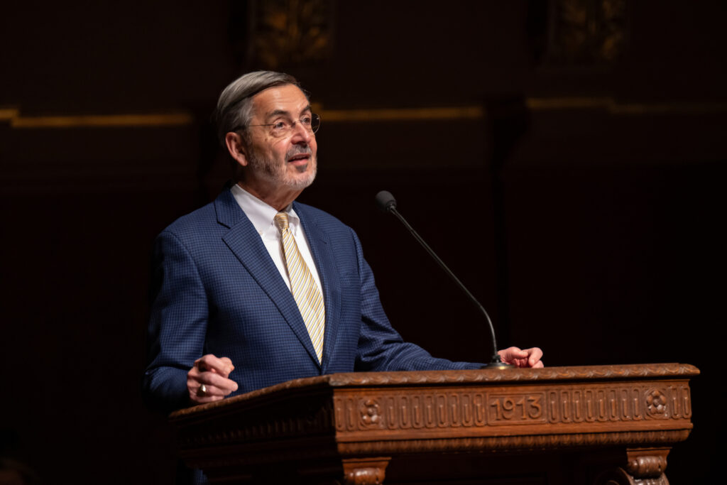 A man wearing a blue suit stands at a podium and speaks