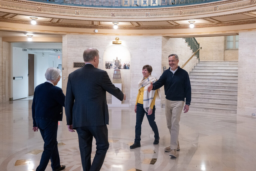 Two couples walk toward each other in an atrium, preparing to shake hands and greet one another