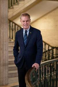 Kent Syverud, caucasian male stands in ornate stairwell wearing Block M tie. 2026.