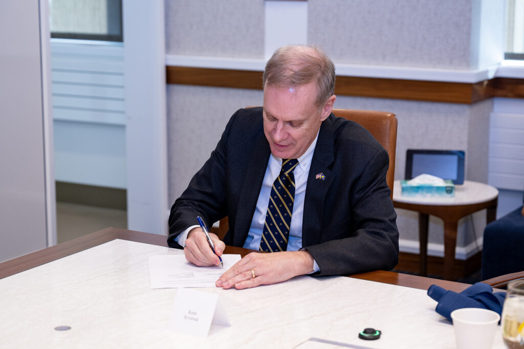 Kent Syverud sits at a table and signs his contract