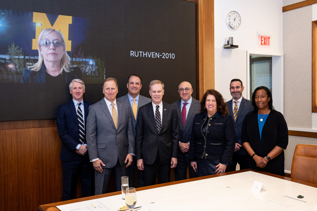 Several people stand side by side with another person appearing on a screen
