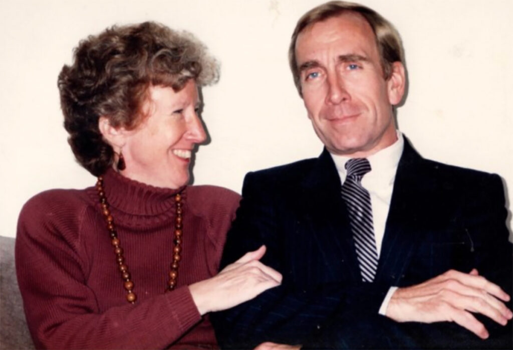 A man and a woman sitting together, with the woman looking and smiling at the man