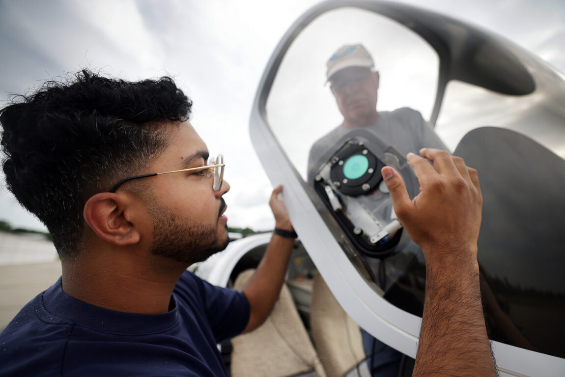 Two men place a sensor inside the window of an airplane cockpit