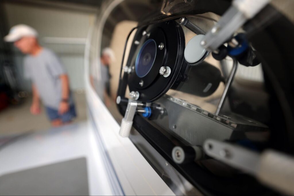 A sensor, which resembles a black cylinder, is mounted inside the window of an airplane cockpit. A flat end of the sensor, which is covered by blue-tinted glass, is approximately level with the window and points out from the cockpit.