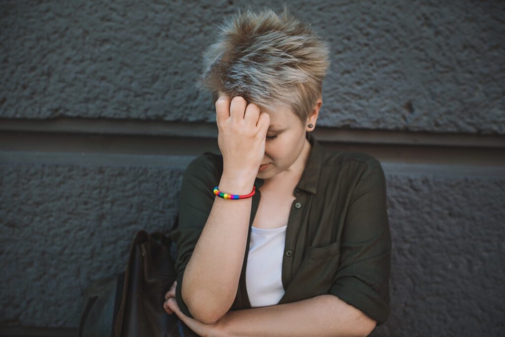 A young person wearing a rainbow bracelet suffering emotional distress. Image credit: Adobe Stock