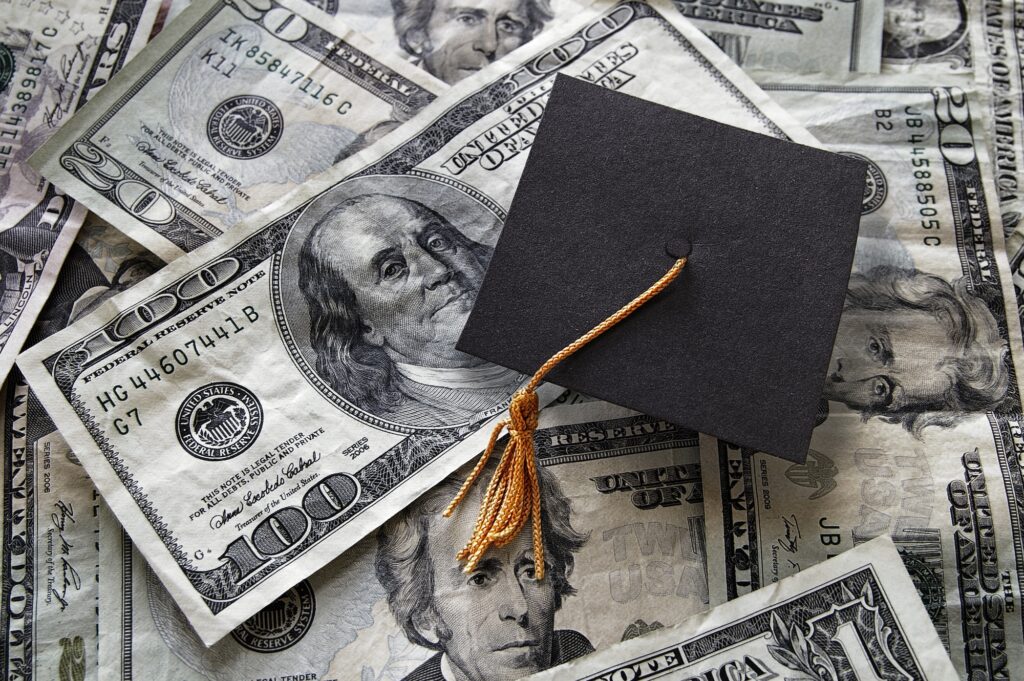Small graduation cap on assorted cash. Image credit: Adobe Stock