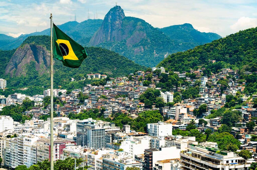 Flag of Brazil with Favela Babilonia, Leme and Corcovado of Rio de Janeiro in the background. Image credit: Adobe Stock
