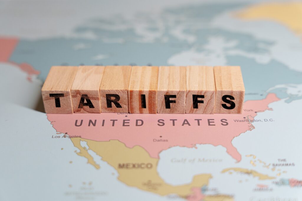 Wooden blocks spelling TARIFFS are placed on a map of North America. Image credit: Adobe Stock